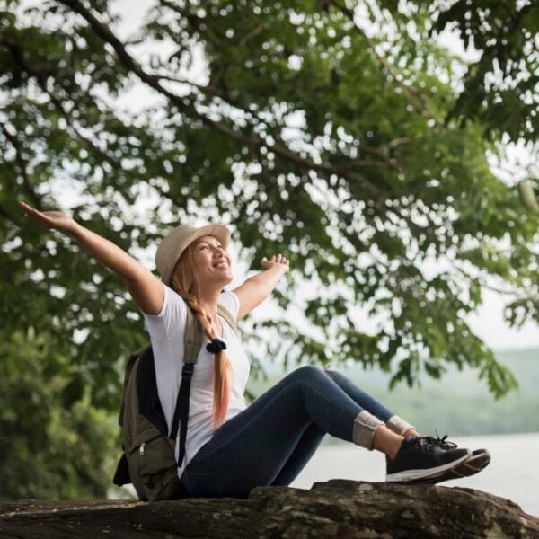 Young happy woman sitting with backpack enjoy the nature after hike. Woman travel concept.